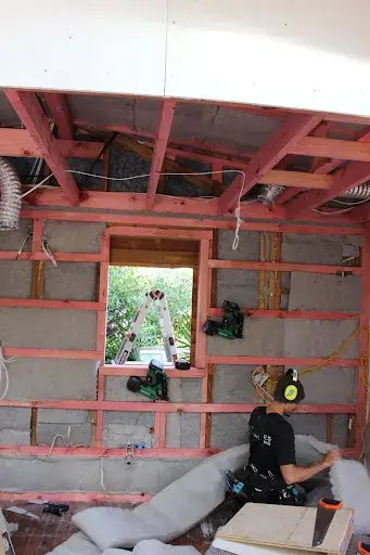 Builder working at a window opening with exposed framing during cladding removal